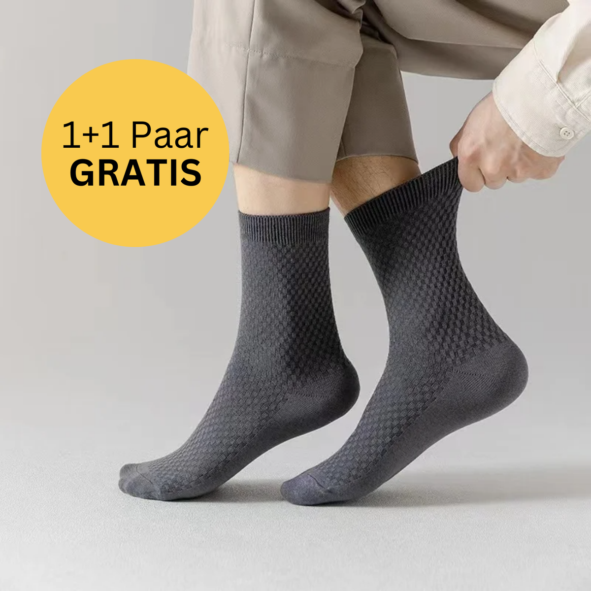 Eine Person trägt Tieberg™ Bambus Socken in Grau mit antibakterieller Wirkung und zieht eine Socke hoch. Neben ihren Beinen steht im gelben Kreis: 1+1 Paar GRATIS. Die Person hat helle Hose und Shirt an.