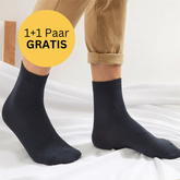 Person trägt Tieberg™ Bambus Socken mit antibakterieller Wirkung und hochgekrempelten beigen Hosen, steht auf weißem Untergrund. Links ein gelber Kreis mit dem deutschen Text "1+1 Paar GRATIS". Marke: Tieberg.