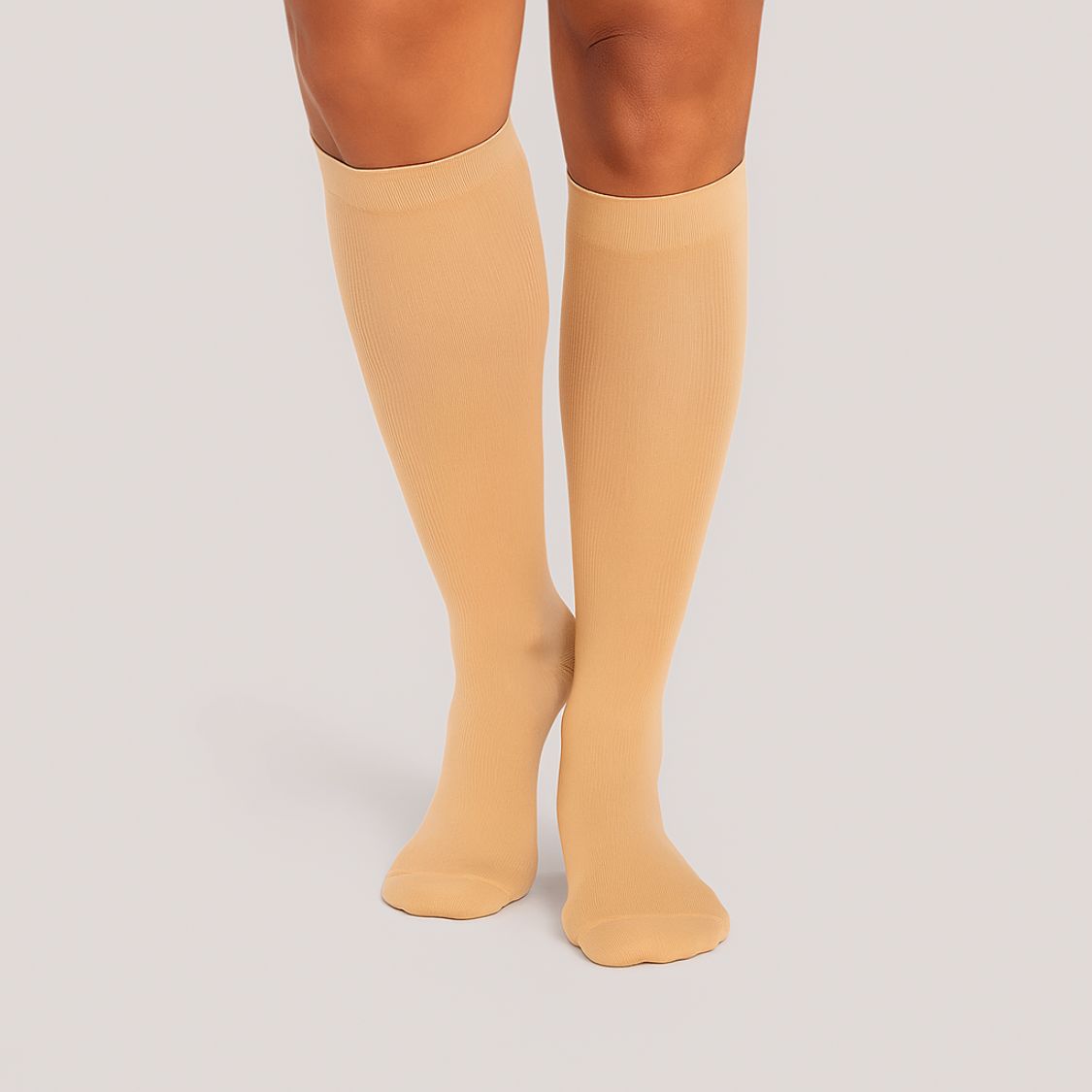 Eine Person, die Tieberg™️ Vitalsocks - Spürbar leichter leben beige Kniestrümpfe trägt, steht auf einer hellen Fläche, die Füße zusammen und die Beine von den Knien abwärts gezeigt.