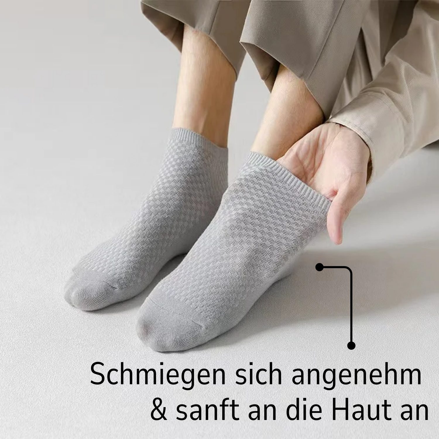 Eine Person trägt hellgraue Tieberg™ Bambus Socken (Kurz), sitzt auf heller Fläche und passt sanft eine Socke an. Unten steht: Angenehm & sanft zur Haut - antibakteriell, von Tieberg.